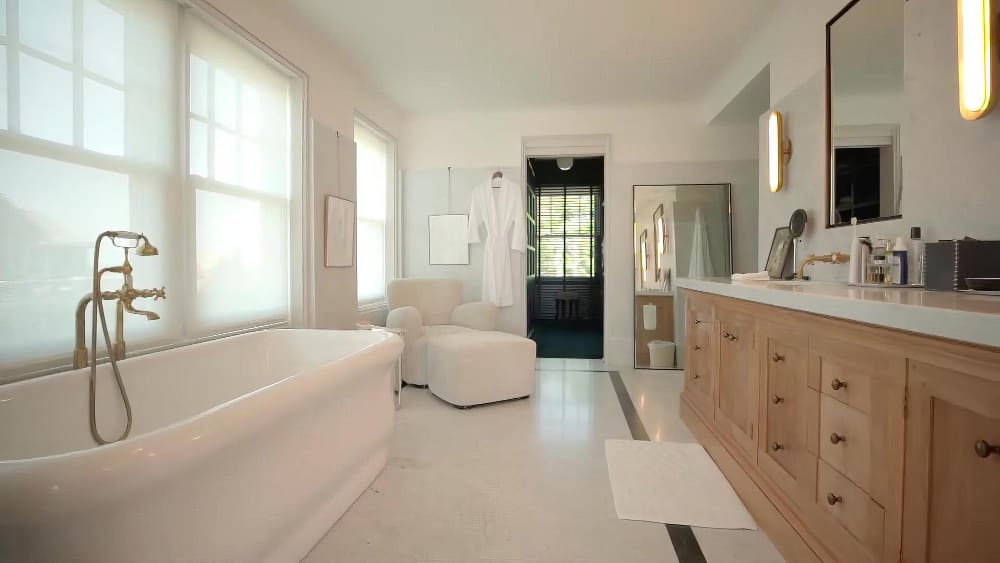 une grande salle de bains avec une baignoire blanche, une grande fenêtre et un meuble sous vasque en bois naturel