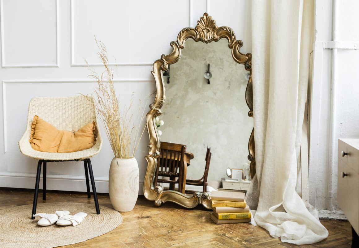 Salon vintage chic avec chaise en osier, grand miroir doré, vase d’appoint, pile de livres et rideau