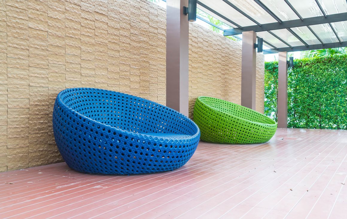 Chaises rondes tissées en rotin synthétique bleu et vert, reposées sur terrasse en bois avec pergola ombragée.