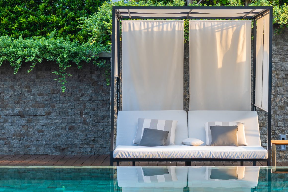 Piscine avec terrasse incluant canapé sous pergola à structure métallique avec rideaux occultants (ombrage latéral et supérieur)