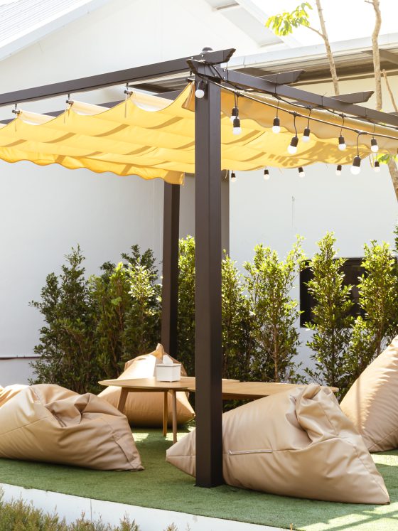 Pergola à toile ondulée avec structure métallique et ombrage léger, coussins confortables et lumière guirlande