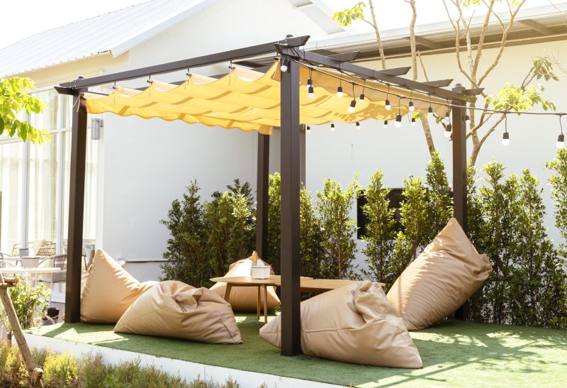 Pergola à toile ondulée avec structure métallique et ombrage léger, coussins confortables et lumière guirlande