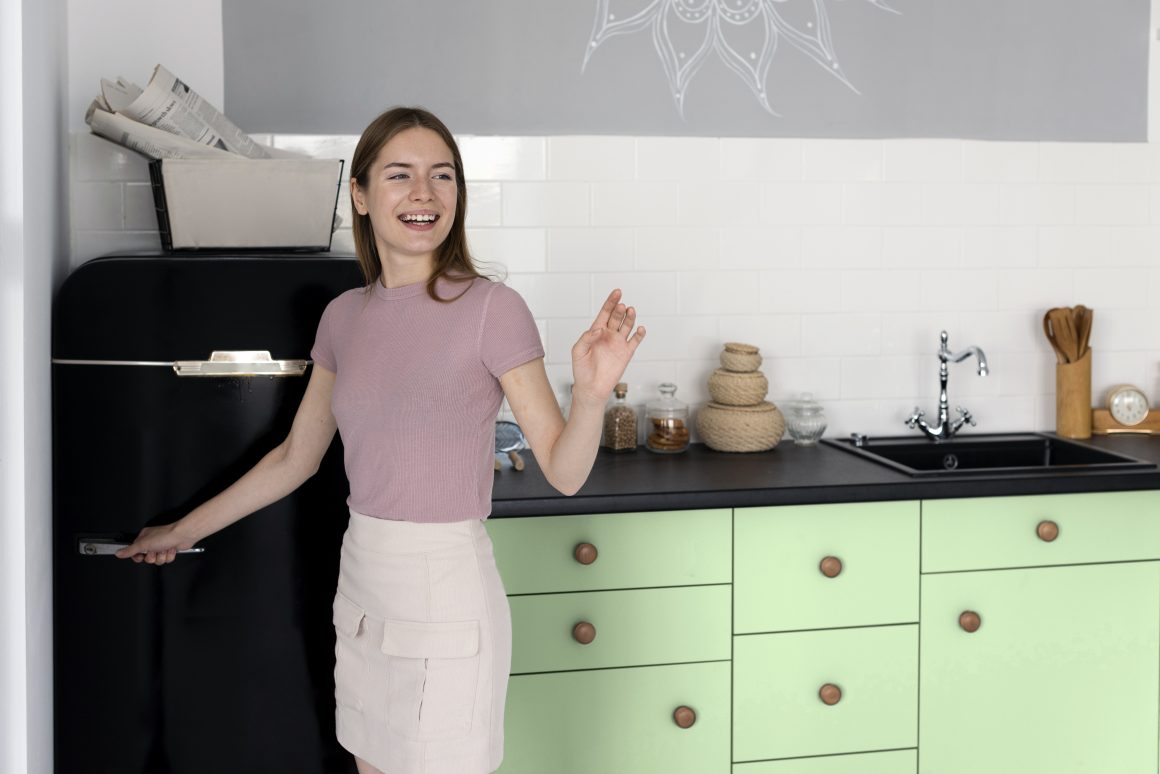 Jeune femme souriante dans une cuisine moderne aux tons pastel, avec des accessoires soignés.