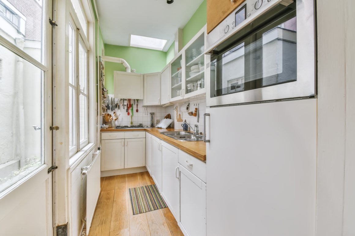 Cuisine étroite avec murs verts, plans de travail en bois, rangements blancs et four encastré.