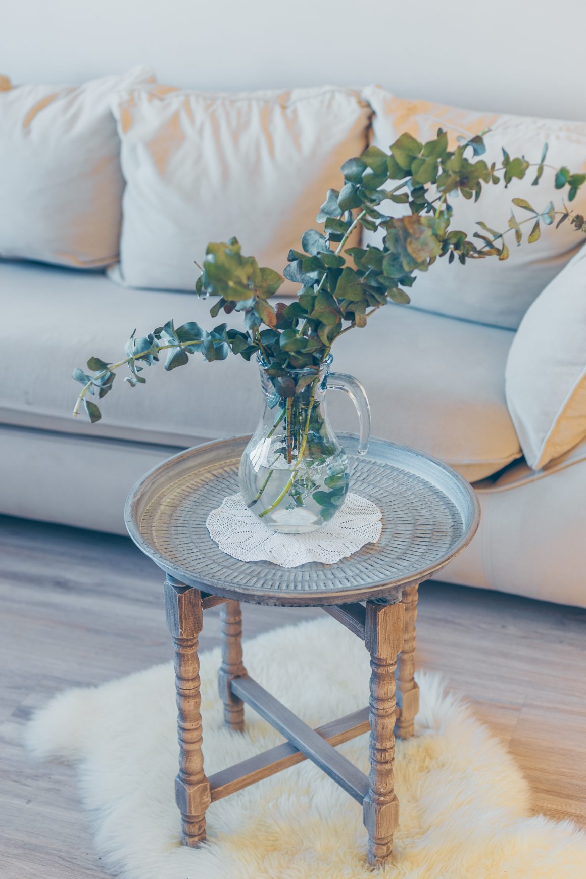 Déco salon vintage moderne avec canapé, table ronde en bois patiné, vase à feuilles vertes et tapis