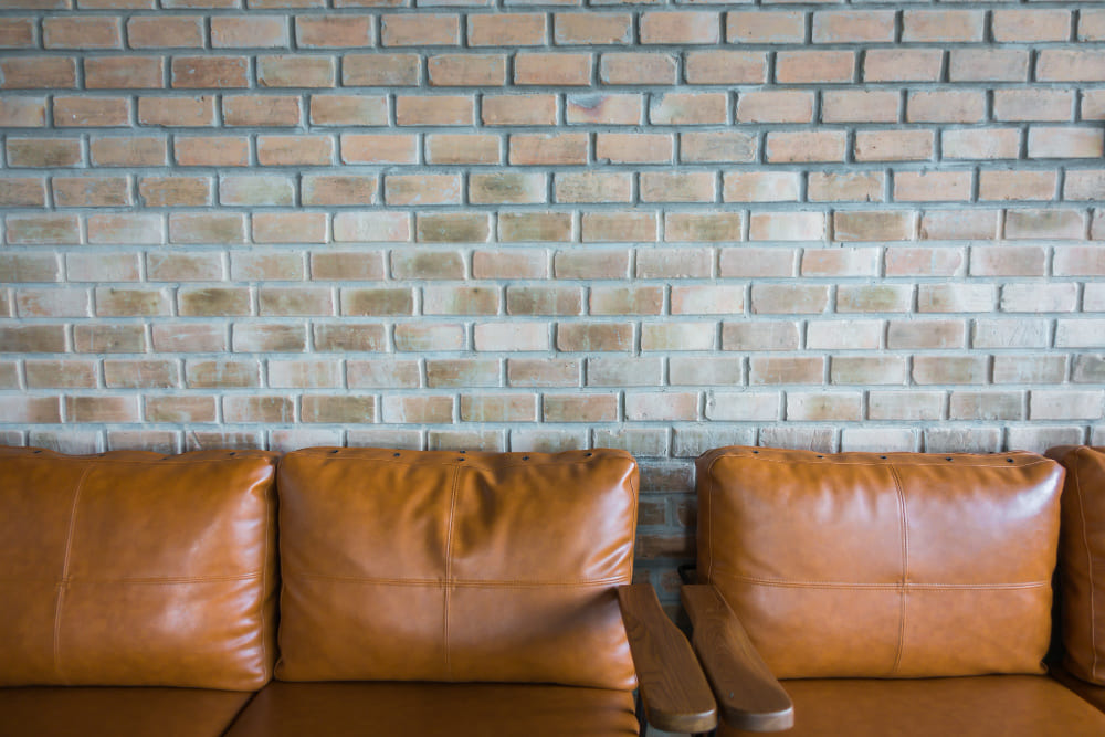 une tapisserie imitant les briques, dans un salon de style vintage, avec un canapé et un fauteuil en cuir