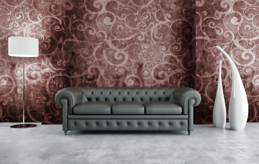 une tapisserie de style baroque dans les tons bordeaux, derrière un canapé gris