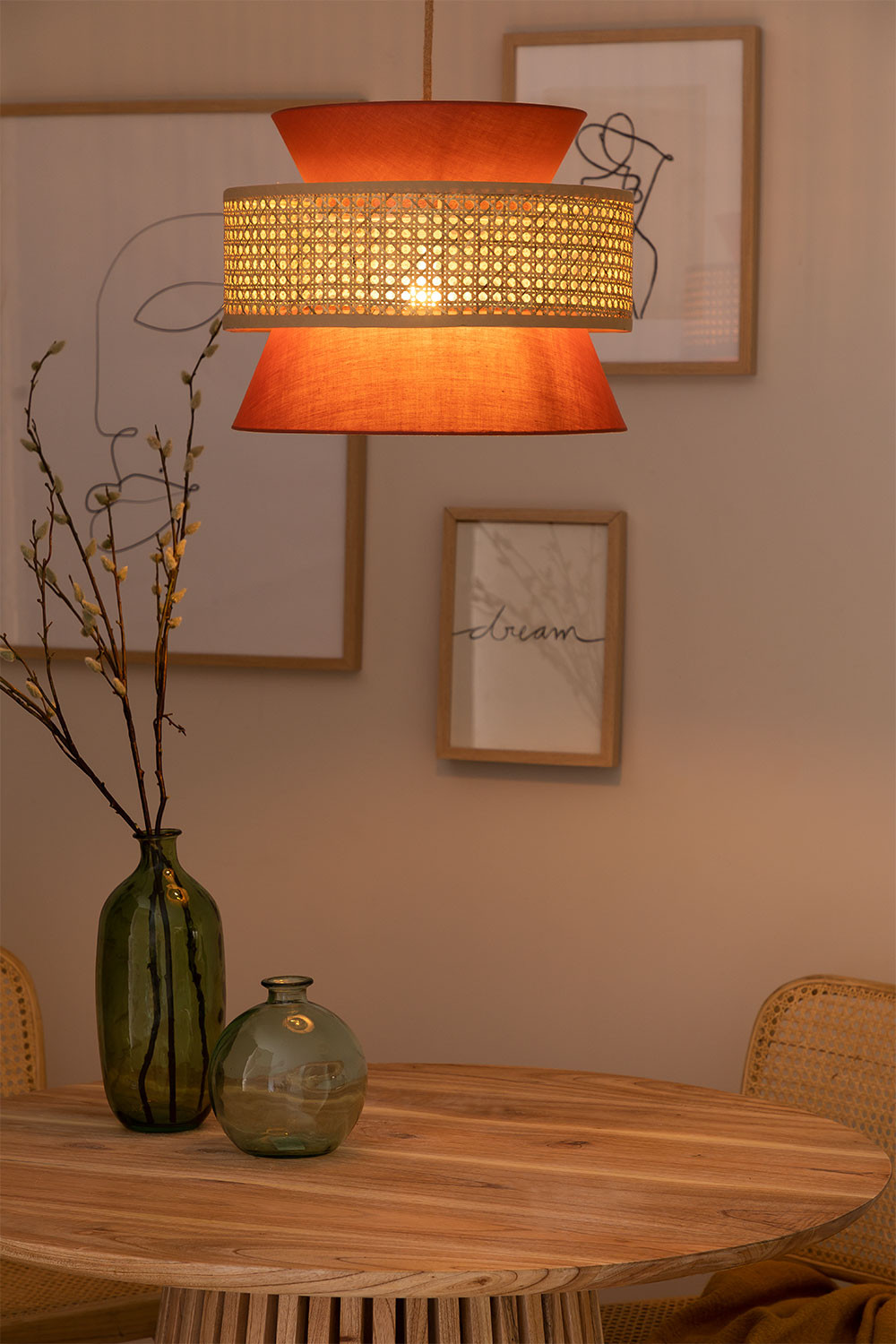 Suspension orange en rotin au-dessus d'une table ronde en bois avec vase vert et chaises cannée