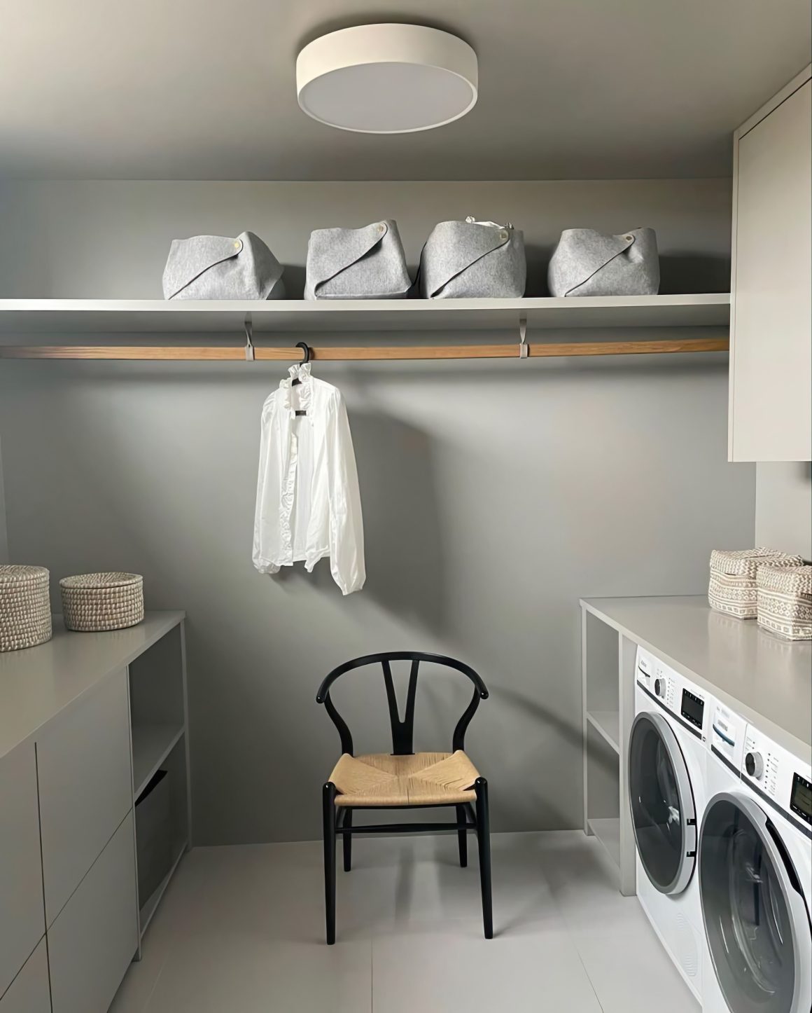 Buanderie en gris clair incluant chaise noire, machine à laver, paniers tressés, étagère avec boîtes