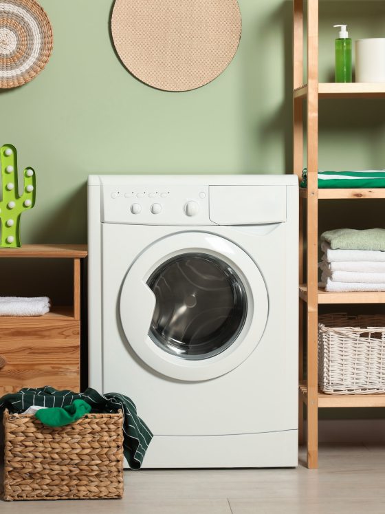 Aménagement garage en buanderie avec lave-linge blanc encadré d'étagères en bois, paniers tressés, serviettes et décor vert apaisant