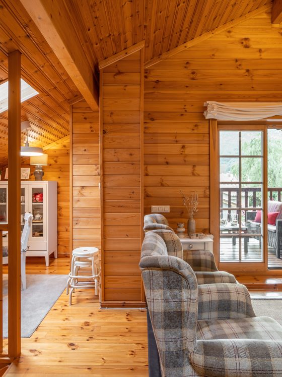Intérieur d'un chalet en bois incluant salon cosy avec fauteuils à carreaux salle à manger avec terrasse