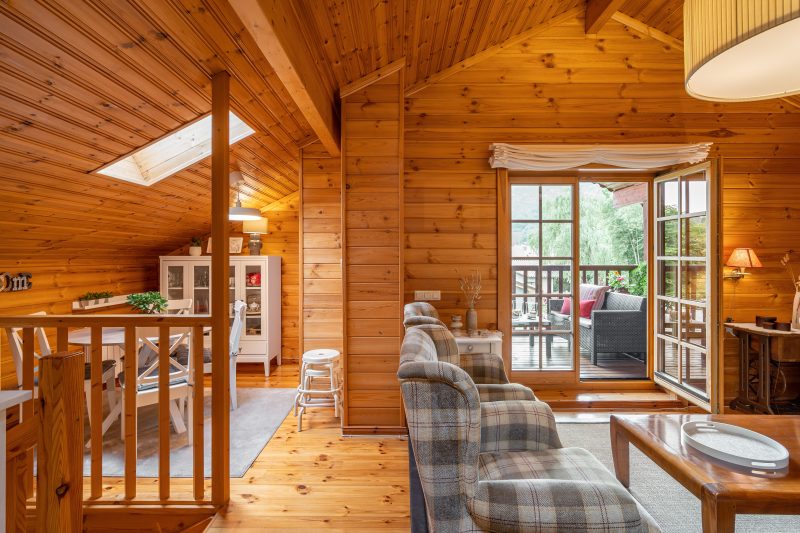 Intérieur d'un chalet en bois incluant salon cosy avec fauteuils à carreaux salle à manger avec terrasse