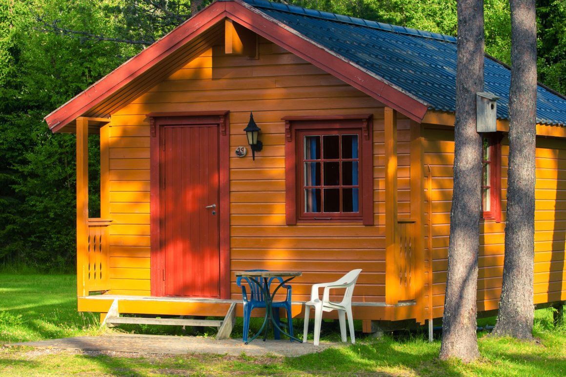 Chalet en bois avec toit bleu, porte rouge, fenêtres marron et salon extérieur simple