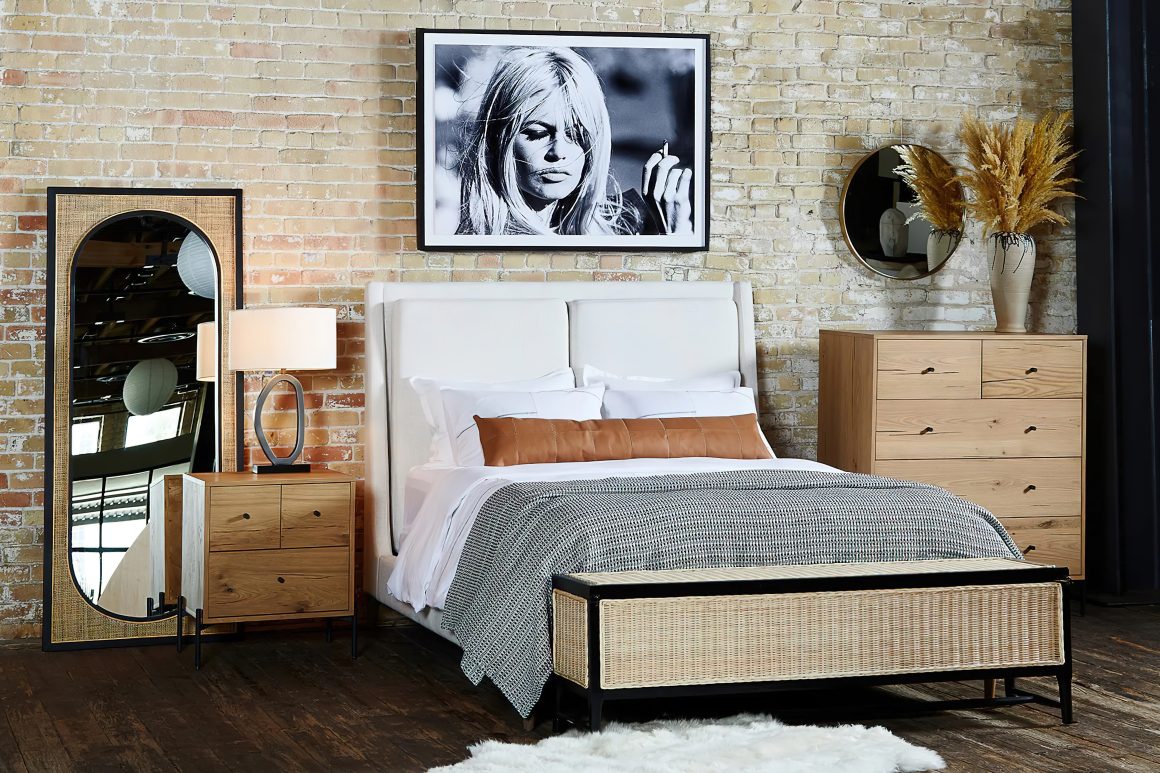 Chambre industrielle : mur en briques, lit blanc, meubles en bois clair, miroir, lampe, plaid gris et tableau noir et blanc.