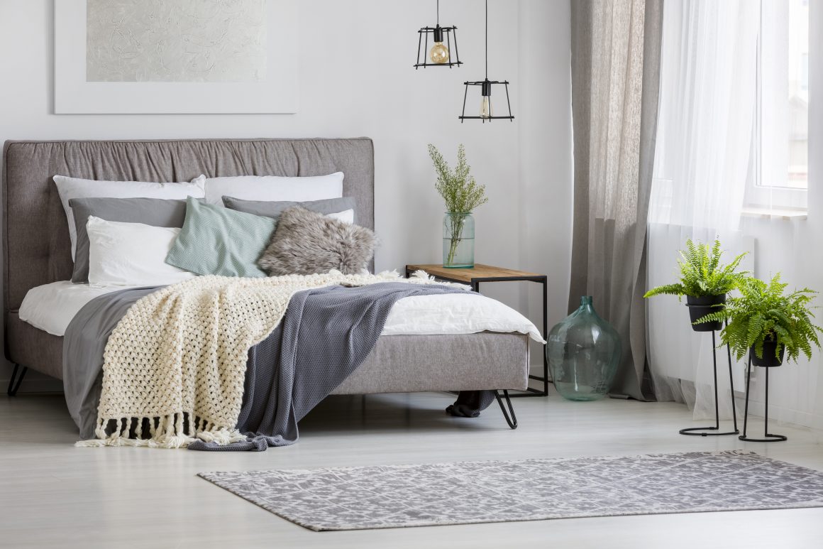 Chambre à coucher incluant lit gris, plaids texturés, plantes vertes, rideaux légers, table d'appoint, suspensions et tapis