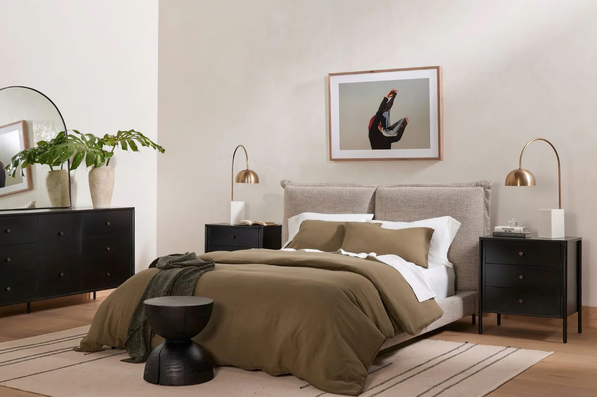Chambre avec lit rembourré, linge olive, chevets noirs, lampes dorées et plante décorative