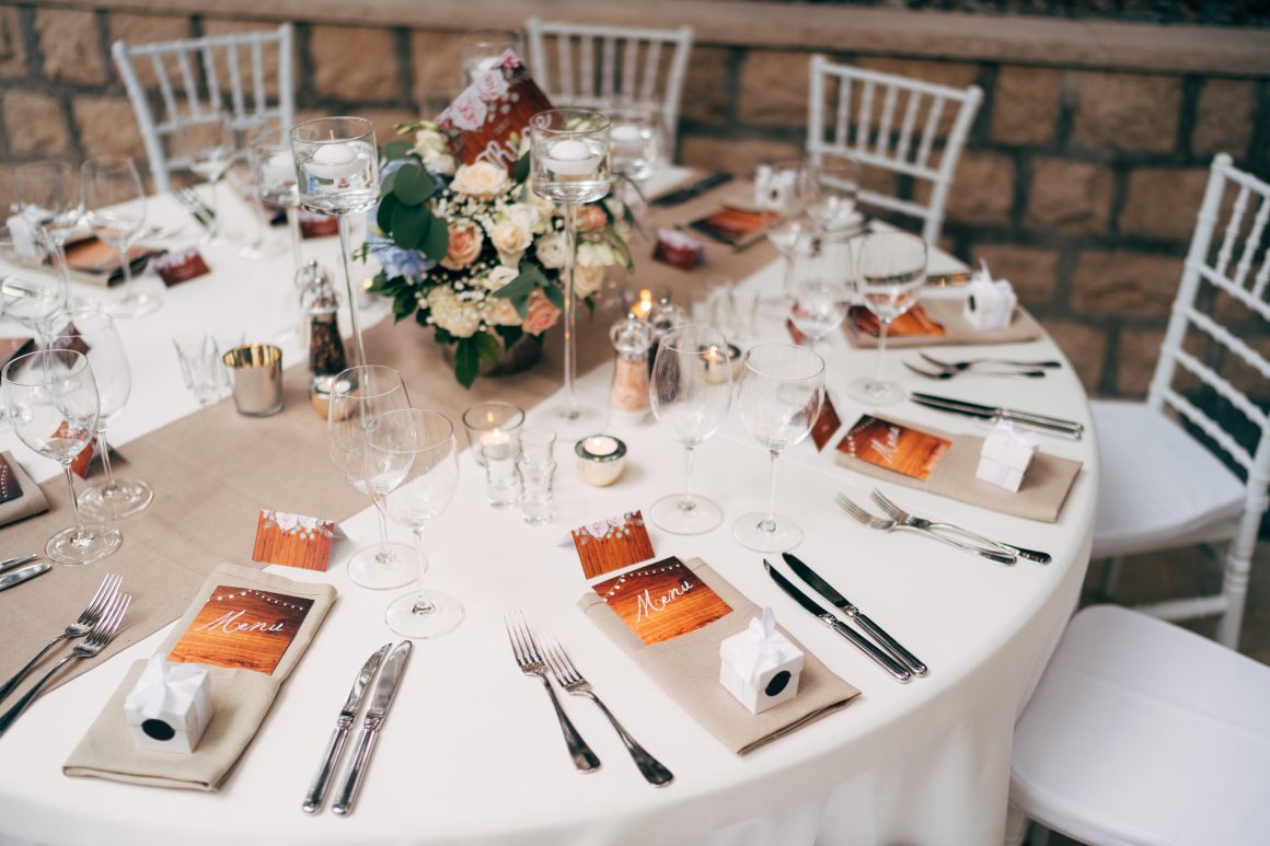 Table dressée élégamment : nappes blanches, verrerie raffinée, bouquets, menus, bougies et chaises Chiavari.
