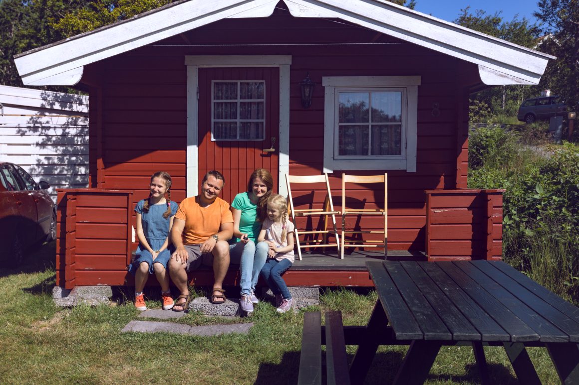 Famille souriante devant petite cabane rouge dans un jardin