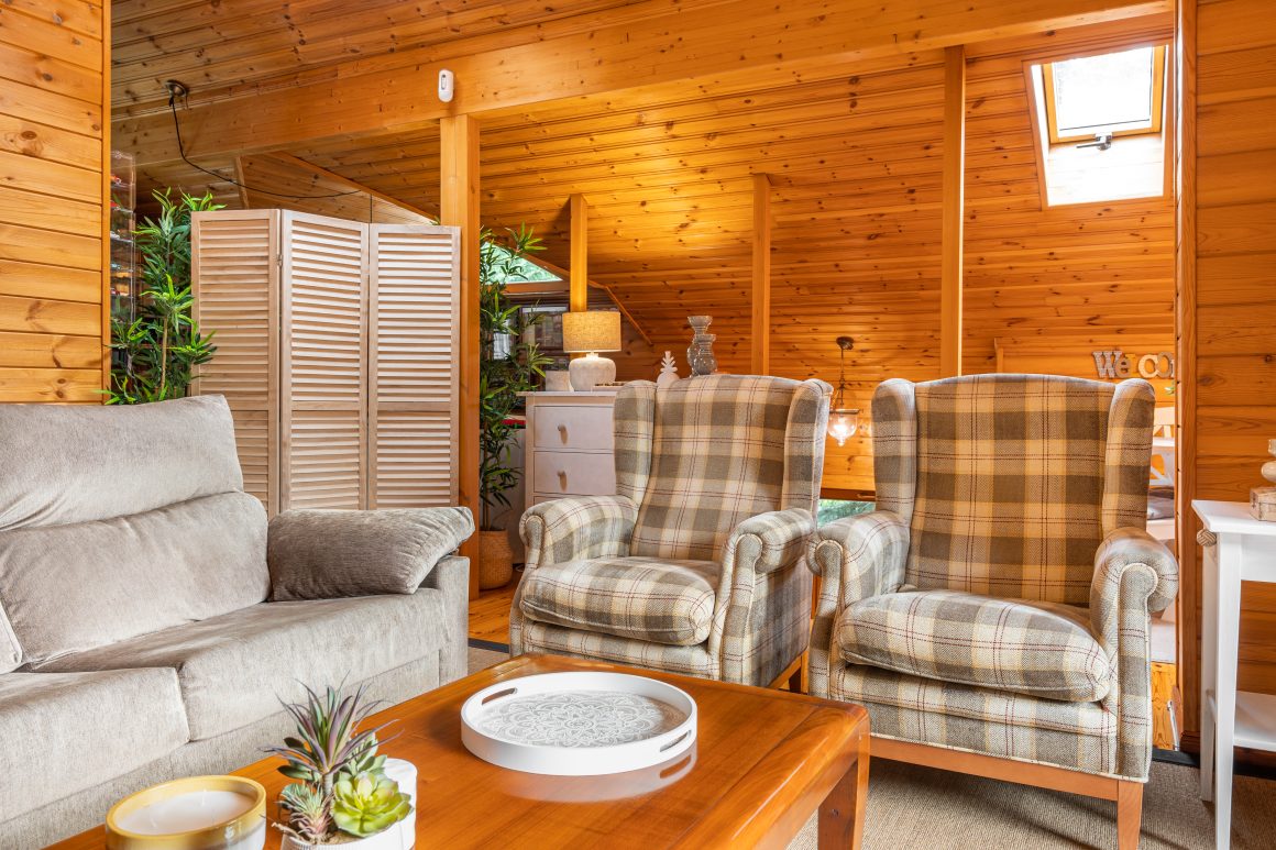 Chalet en bois habitable avec salon cosy incluant canapé, fauteuils, table basse, plantes et paravent