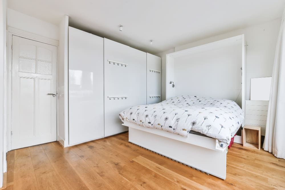 un lit deux places dépliant blanc, avec une grande penderie à côté, et du parquet au sol