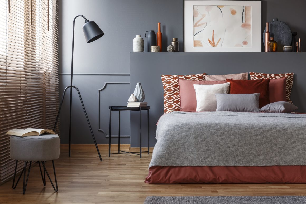 Chambre aux tons gris et terracotta avec literie moelleuse, lampadaire sur pied, table basse et déco minimaliste