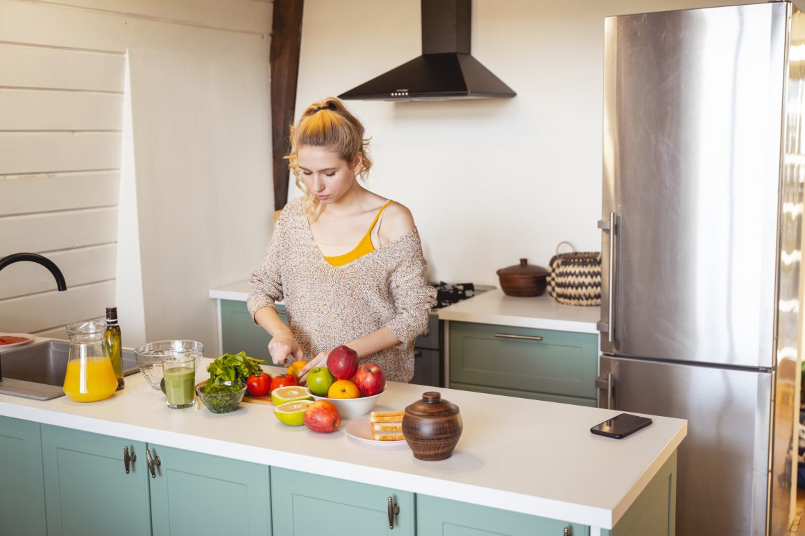 Jeune femme préparant le repas dans une petite cuisine incluant îlot central avec évier et placards