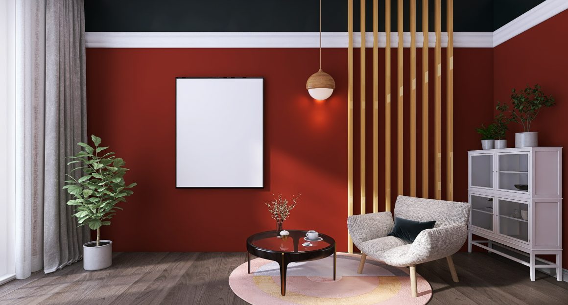 Salon avec murs rouges, plafond sombre, mobilier gris clair, fauteuil, table basse ronde, tapis multicolore et plantes.