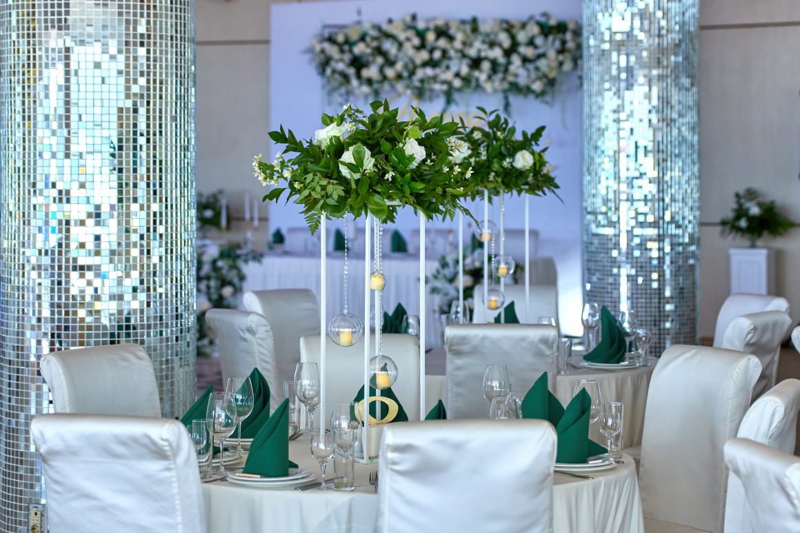 Tables élégantes avec nappes blanches, chaises satinées, centres floraux verts et blancs et bougeoirs suspendus