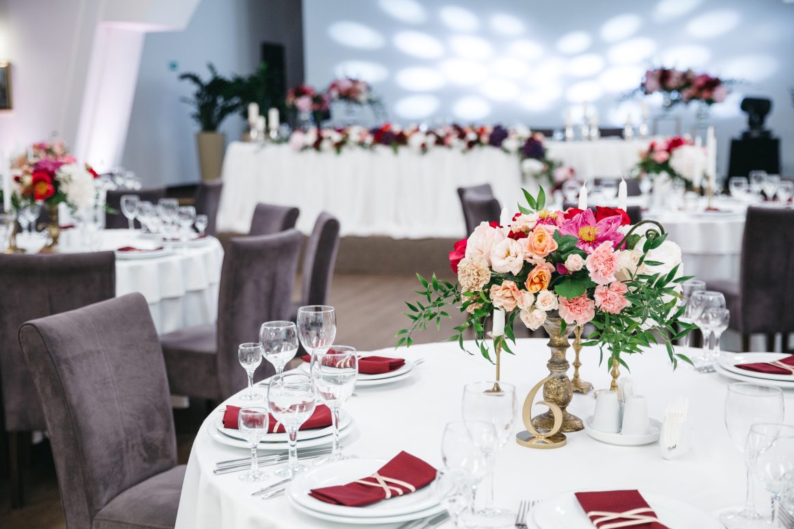 Salle élégante de réception avec tables rondes nappées, centres floraux roses et rouges et verres scintillants