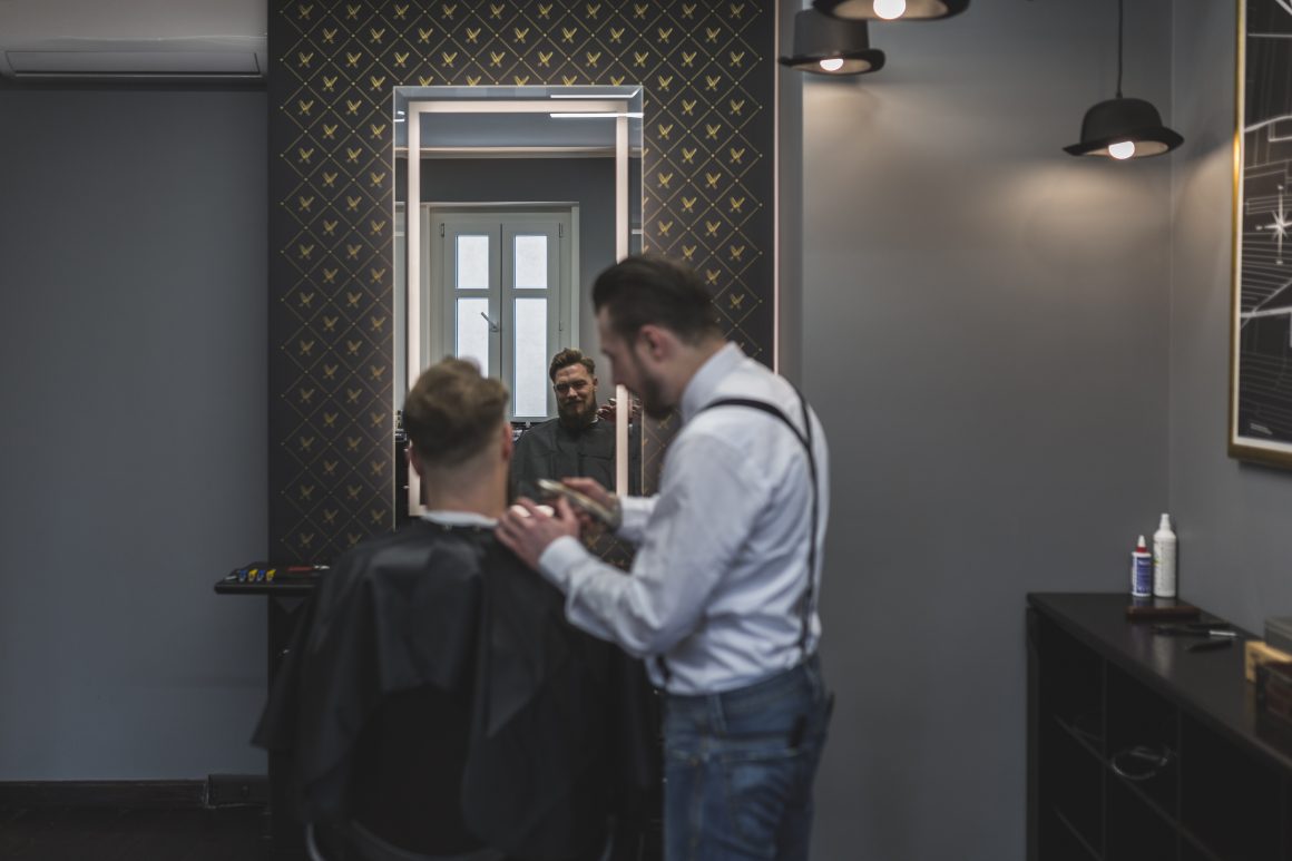 Un coiffeur coiffant un client dans un salon moderne avec mur gris, miroir et lumière douce