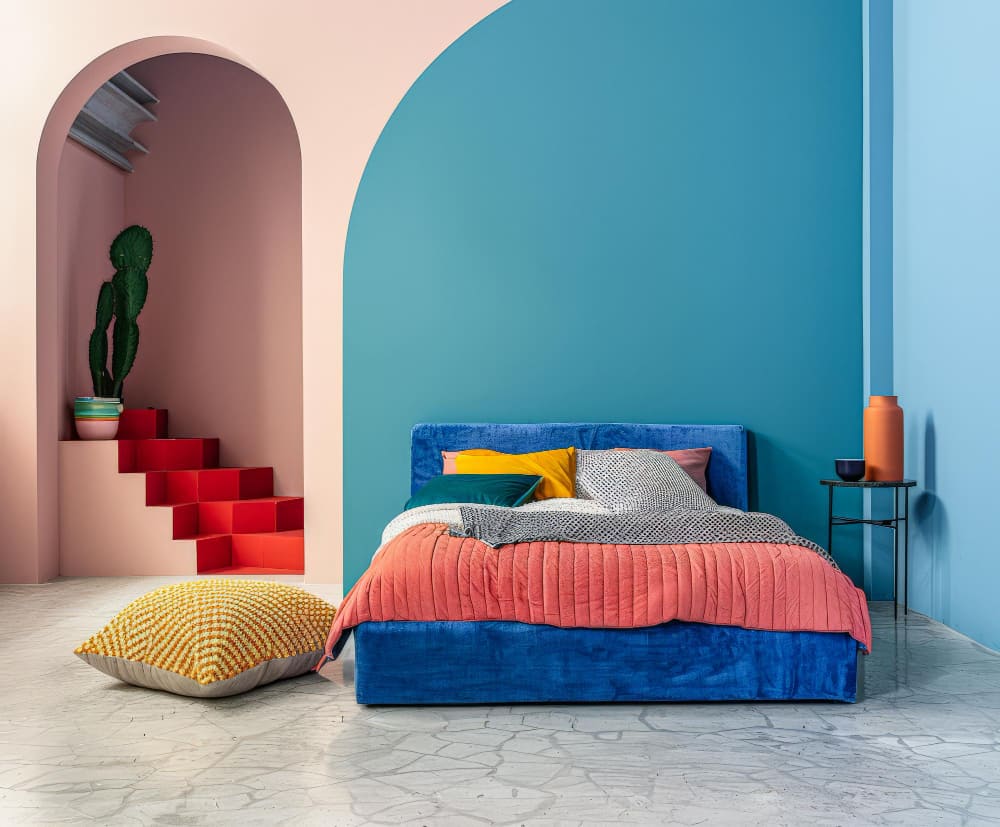 Un bel aperçu de la tendance déco chambre adulte avec du bleu au-dessus du lit, un édredon rose et un escalier rouge