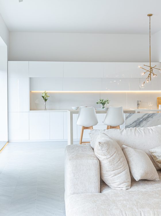 Cuisine ouverte sur salon incluant îlot marbre, mobilier épuré, suspensions dorées et grand canapé