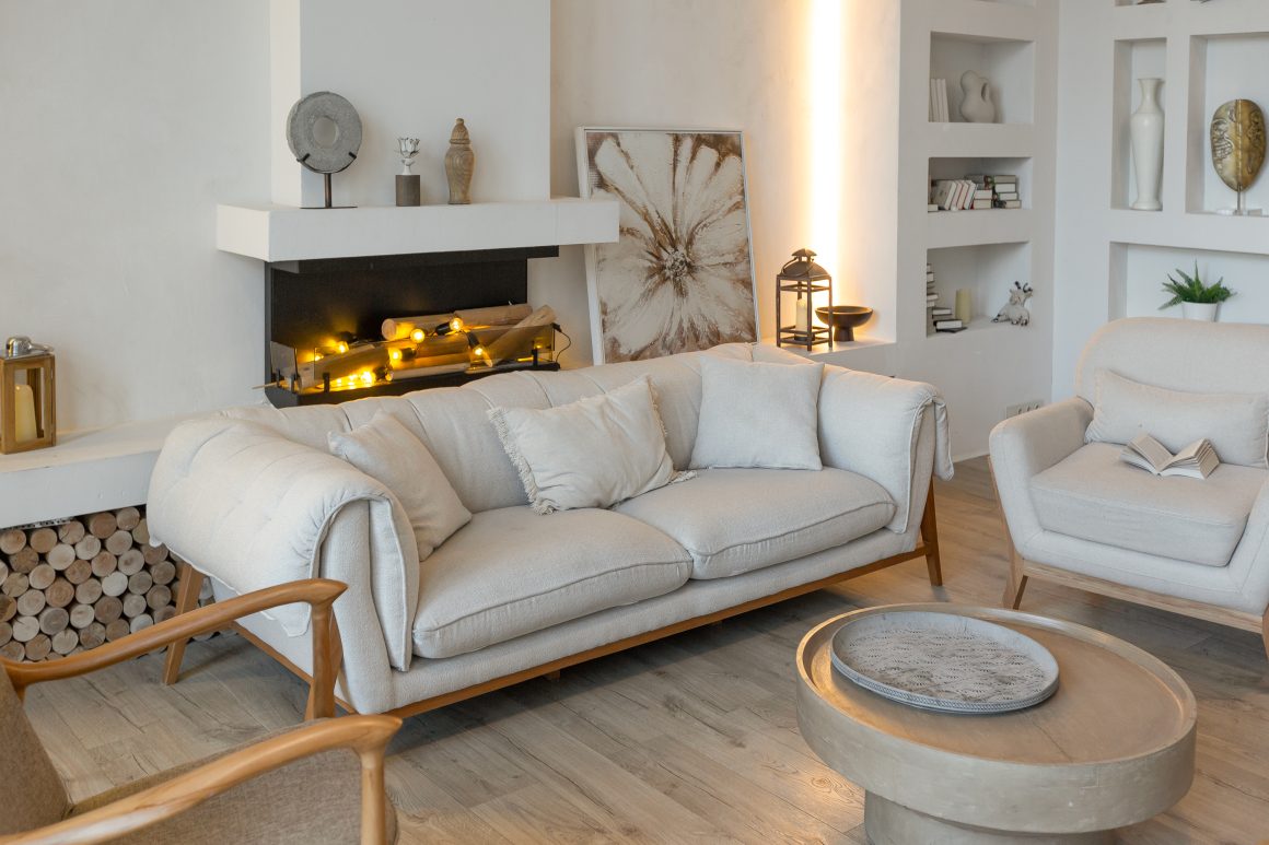Séjour avec cheminée, canapé gris clair, fauteuils, table basse et étagères murales avec livres et objets déco