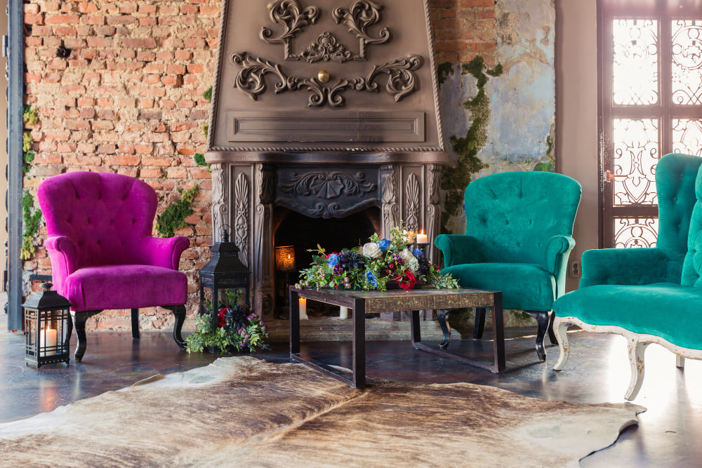 une cheminée ancienne dans un grand salon authentique et trois fauteuils aux couleurs vives turquoise et rose