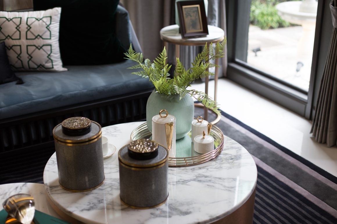 Table basse ronde en marbre avec objets décoratifs: pots gris, lueur dorée, vase vert et plantes.