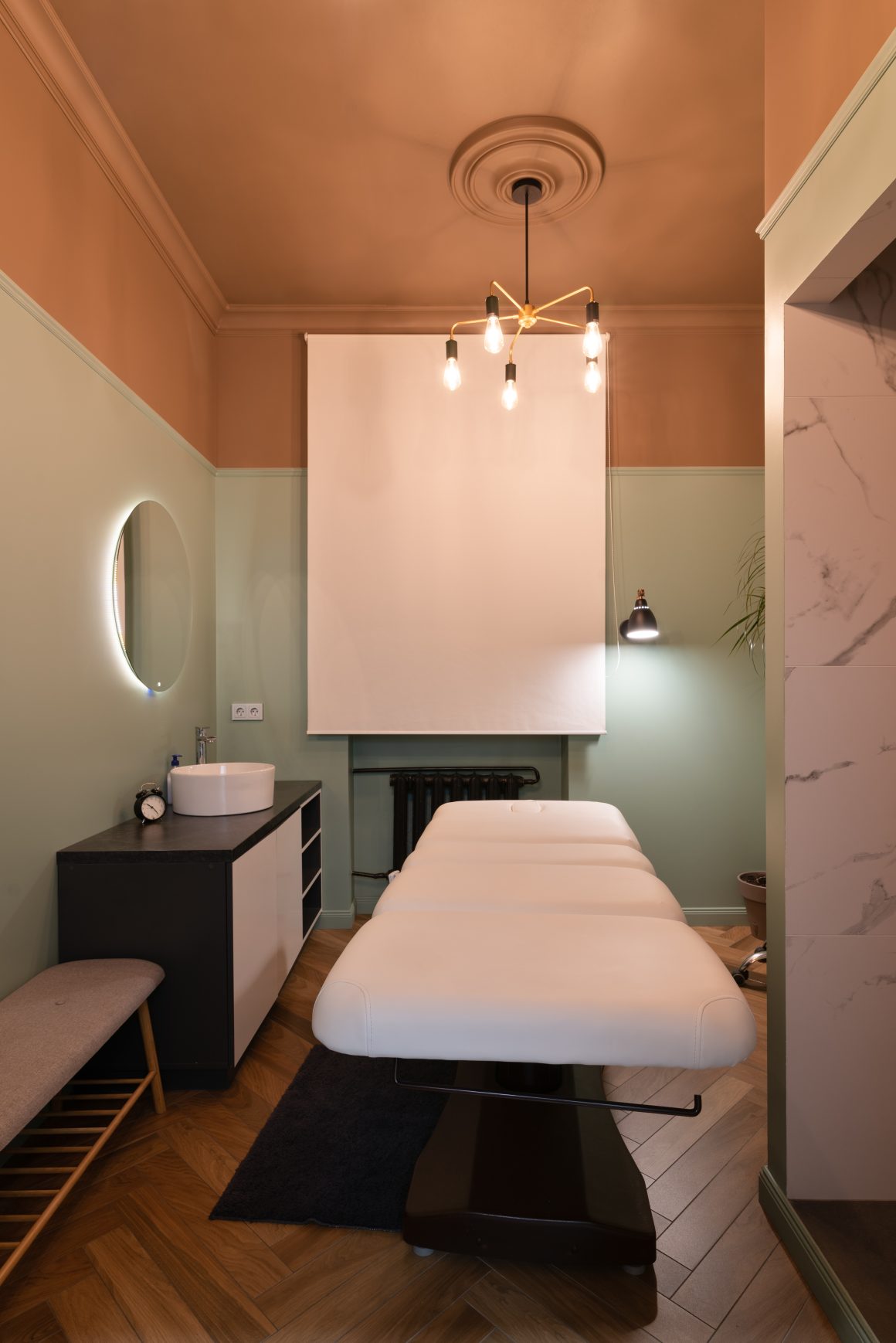 Salle de massage incluant table blanche, éclairage chaleureux, murs verts et plafond terracotta.