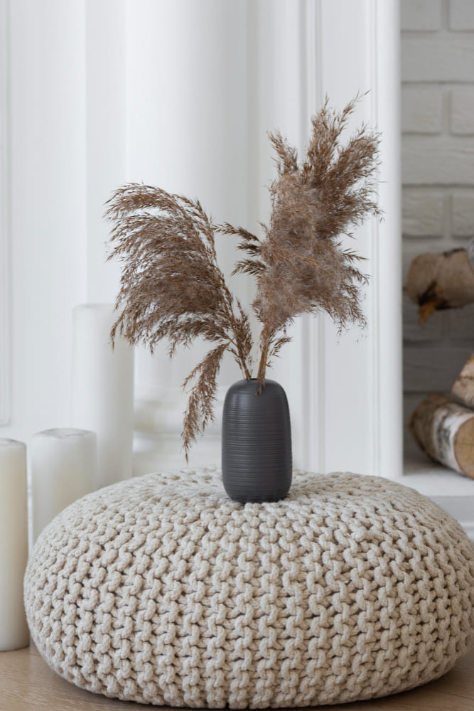 un gros pouf en laine épaisse, avec un pot en grès avec des plantes séchées