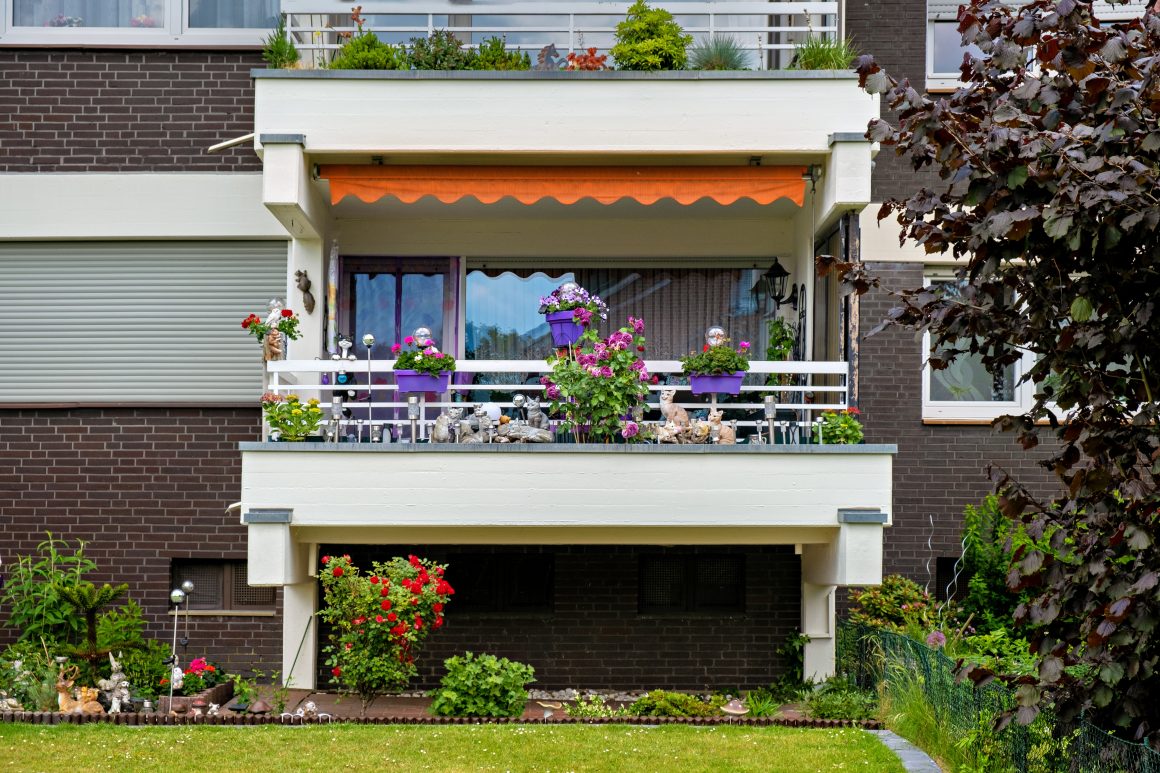 Balcon fleuri sur façade sombre avec store, jardinières colorées et plantes