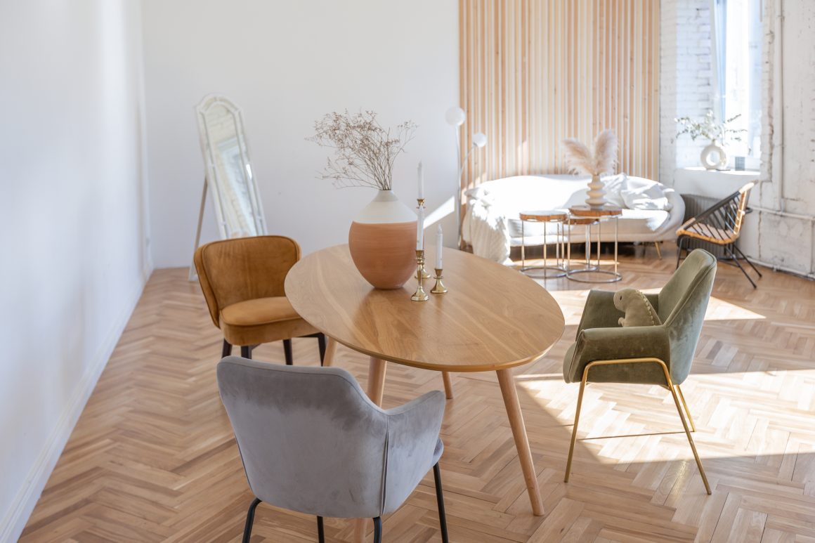 Table ronde en bois clair au centre avec chaises pastel et vertes, miroir, vase et bougies