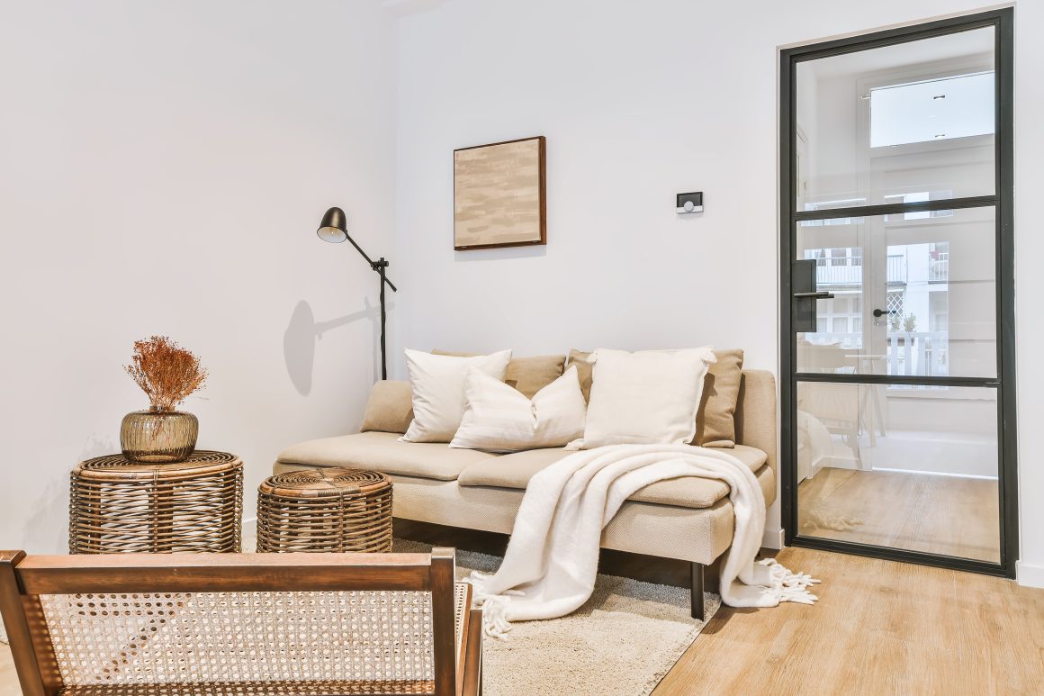Petit salon incluant canapé beige avec plaid, lampe noire, fauteuils en rotin et tapis