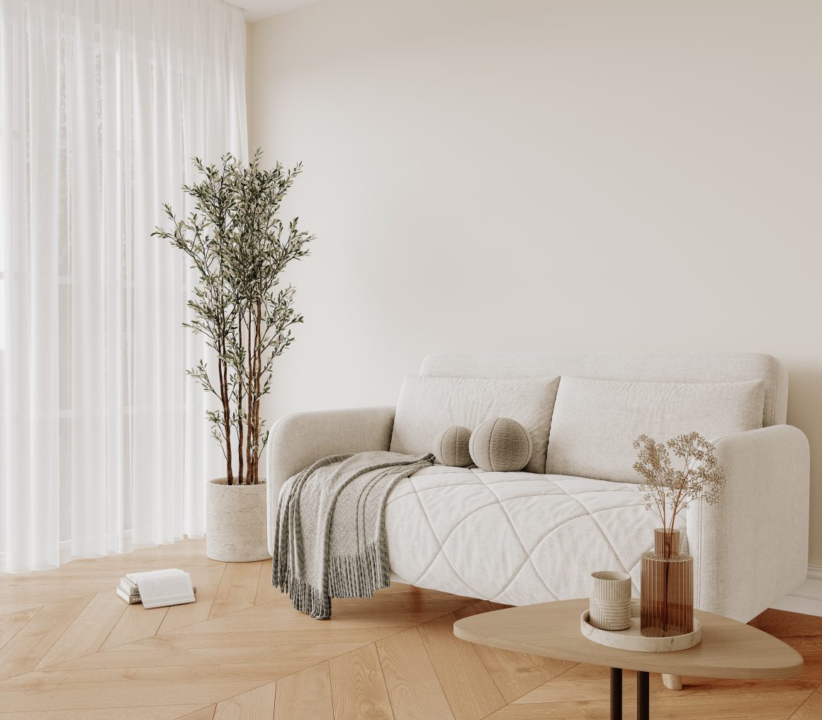 Canapé beige avec plaids et coussins ronds, table basse ovale, plantes et lumière naturelle.
