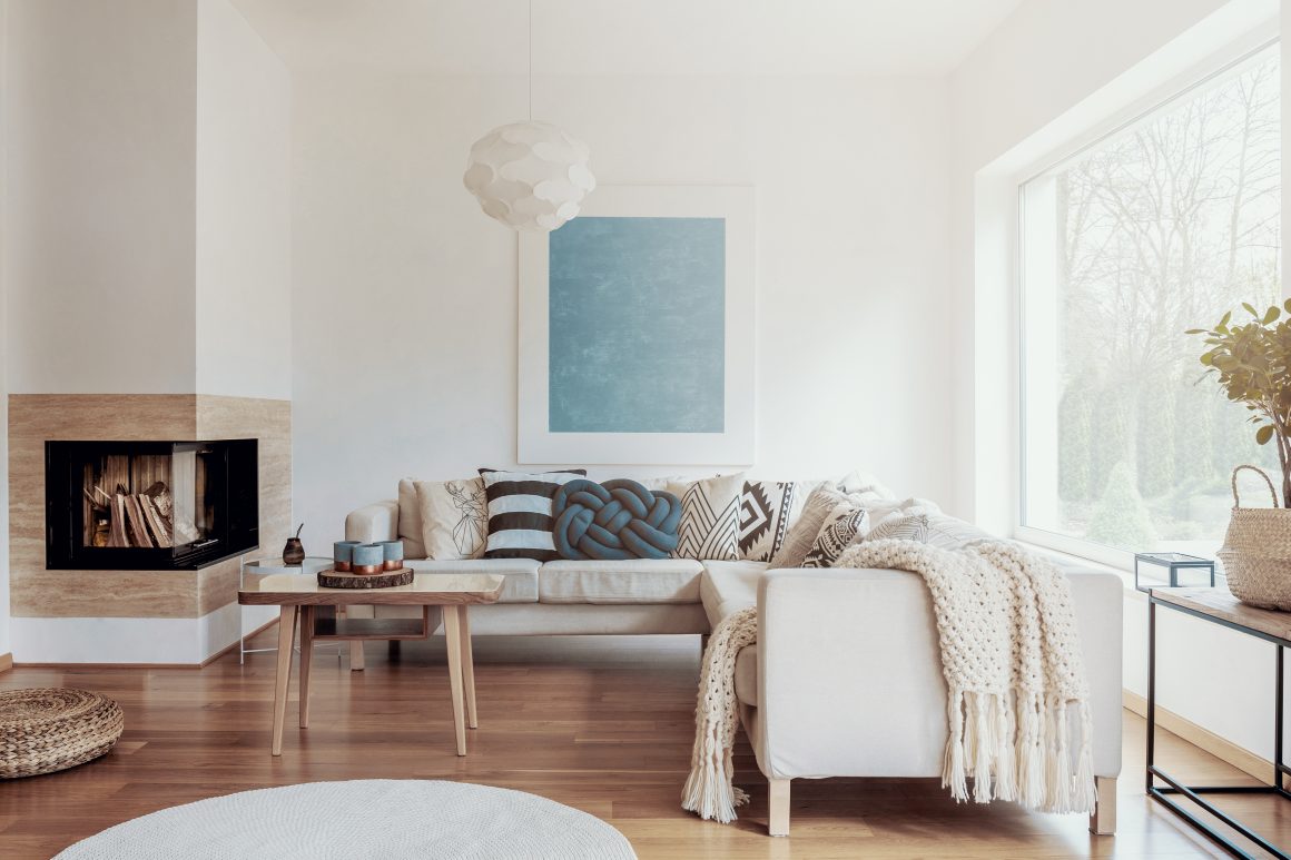 Salon lumineux avec cheminée moderne, canapé beige, tapis rond, grande baie vitrée et table basse en bois