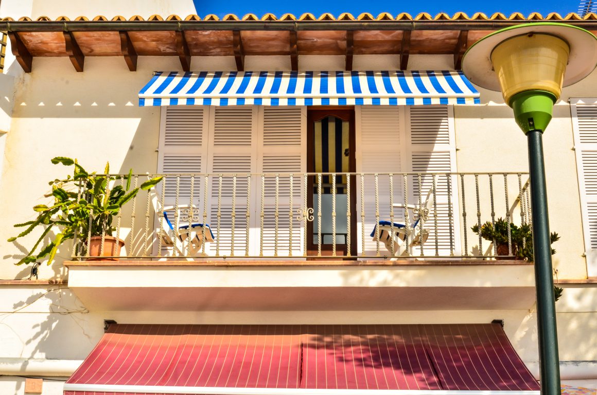 Balcon lumineux avec store rayé bleu et plantes en pot