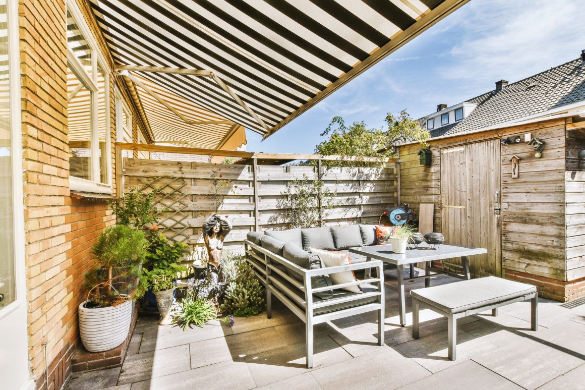 Terrasse ensoleillée incluant mobilier moderne gris, plantes en pots, statue décorative et store rayé