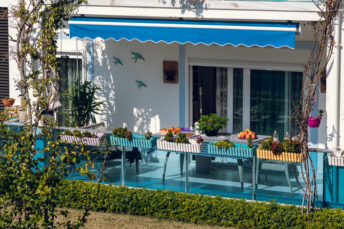 Terrasse ensoleillée incluant plantes en pots, chaises colorées et store bleu