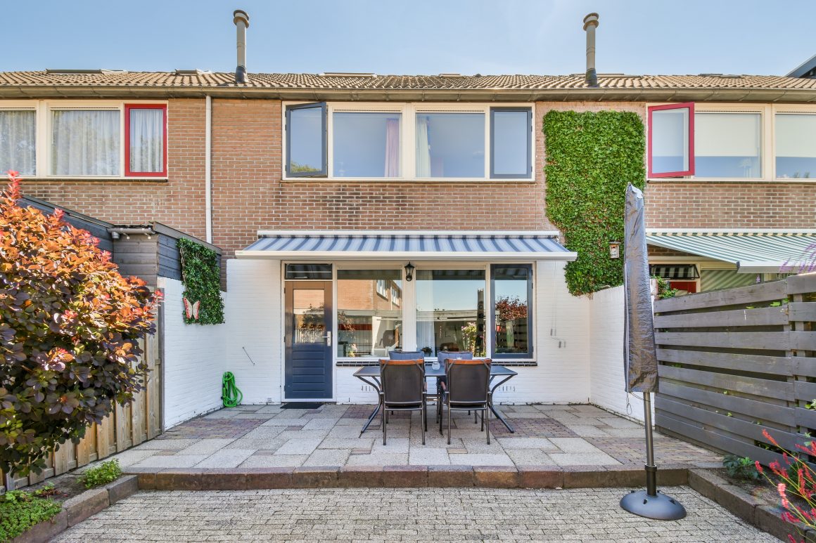 Terrasse avec table et chaises noires, store à rayures et plantes grimpantes