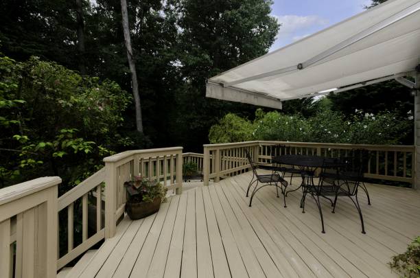 Spacieuse terrasse en bois beige avec table, chaises métalliques et store blanc déployé