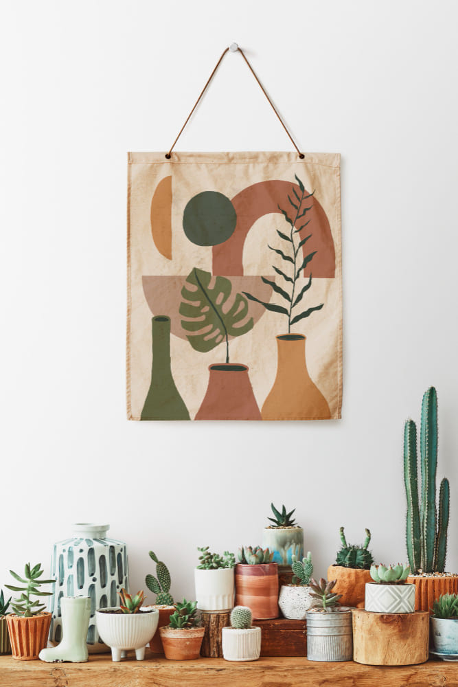 un tableau en lin peint suspendu au mur, au-dessus d'une étagère ornée de cactus