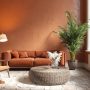 Tendance déco salon dans les tons terracotta, avec une table basse en osier, un canapé chaleureux et une plante verte