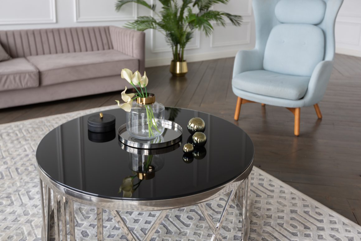 Table basse ronde noire avec vase transparent, plantes, boules dorées et plateau miroir.